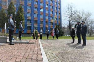 Zdjęcie kolorowe. Widoczni umundrowani policjanci przez Grobem Policjanta Polskiego na terenie KWP w Katowicach, w tym Komendant Wojewódzki Policji w Katowicach