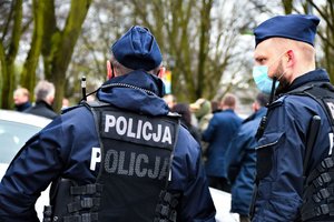 Policjanci stojący jeden tyłem, drugi bokiem.