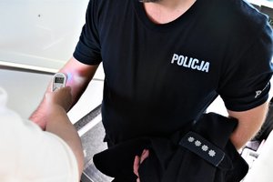 Kobieta przykłada termometr do ręki policjanta, który zamierza oddac krew.