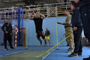 Zdjęcie kolorowe. Rekruci podczas skoku w dal z miejsca i policjanci prowadzący selekcję