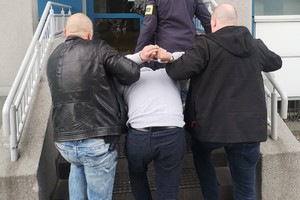 Policjanci prowadzą zatrzymanego mężczyznę.
