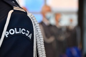 Zdjęcie kolorowe. Zbliżenie na ramie policyjnego munuduru z napisem POLICJA