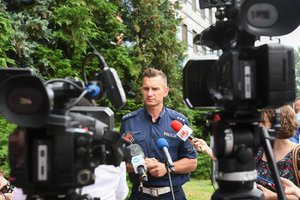 Zdjęcie kolorowe. Briefing prasowy przed komendą wojewódzką policji, przed mikrofonami głos zabiera umundurowany policjant