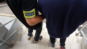 Policjant prowadzi zatrzymanego mężczyznę trzymając go za ramię.