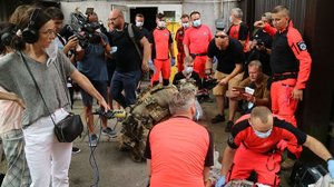 Ratownicy i kontrterroryści podczas ćwiczeń udzielają pomocy poszkodowanemu. W tle stoją dziennikarze.