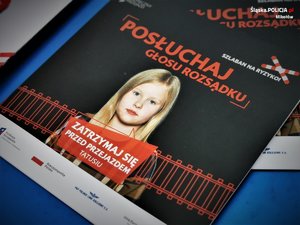 Zdjęcie kolorowe. Widoczny fragment radiowozu oznakowanego oraz ulotki kampanii profilaktycznej