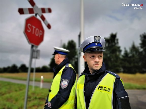 Zdjęcie kolorowe. Widoczny umundurowany policjant obok torowiska kolejowego