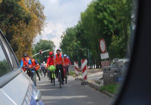 Kolorowa fotografia przedstawia rowerzystów, których widać w lusterku bocznym radiowozu.