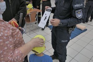 Zdjęcie kolorowe. Widoczny umundurowany policjant, który na terenie sklepu wręcza gadżet osobie