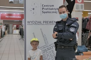 Zdjęcie kolorowe. Widoczne dzaiecko na terenie sklepu obok policjanta