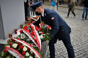 Kolorowa fotografia. Umundurowany policjant składa wieniec kwiatów pod pomnikiem.