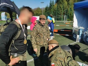 Zdjęcie kolorowe: policjant z medalem na szyi, wokół inni uczestnicy maratonu