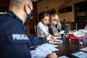 Z lewej policjant a w dalszym planie dwie  dziewczynki podczas tworzenia śiątecznych kartek.