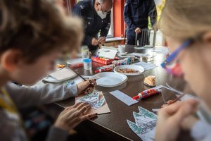 Policjanci przy stole tworzą kartki świąteczne wraz z dziećmi.