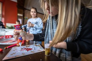 Dzieci tworzą kartki świąteczne. Na pierwszym planie dziewczynka która zdobi swoją pracę.