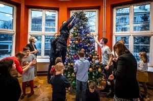 Umundurowany policjant zawiesza gwiazdkę na choince. Obok świątecznego drzewka stoją i siedzą dzieci z Domu Dziecka w Katowicach.