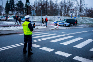 Umundurowany funkcjonariusz policji kierujący ruchem, w tle oznakowany radiowóz policji