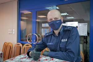 Umundurowany policjant oparty o spakowane w ozdobny papier pudełko z uniesionym do góry kciukiem.