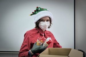 Pracownica cywilna w świątecznej czapce. Trzyma w dłoni artykuły spożywcze.