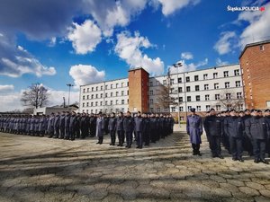 Zdjęcie kolorowe. Widoczni umudurowani policjanci na placu podczas ślubowania