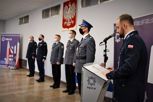 Na pierwszym planie lektor, w tle umundurowani przedstawiciele kadry kierowniczej i baner z napisem Policja.