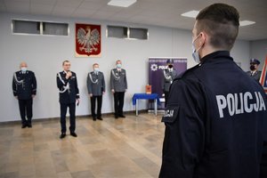Na pierwszym planie umundurowany, nowo przyjęty policjant, w tle Komendant Wojewódzki Policji podczas przemówienia.