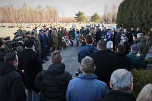 Widoczni uczestnicy uroczystości, mundurowi i cywile na terenie cmentarza