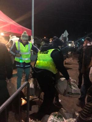 Na zdjęciu widać umundurowanych policjantów oraz obcokrajowców. Mundurowi pomagają uchodźcą w pakowaniu bagaży do autobusów.