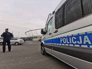 Zdjęcie kolorowe. Widoczne policyjne radiowozy i policjanci obok stadionu