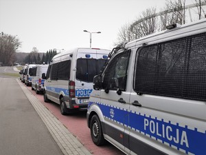 Zdjęcie kolorowe. Widoczne policyjne radiowozy i policjanci obok stadionu