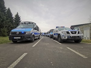 Zdjęcie kolorowe. Widoczne policyjne radiowozy i policjanci obok stadionu