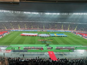 Zdjęcie kolorowe. Widoczny stadion i piłkarze oraz kibice