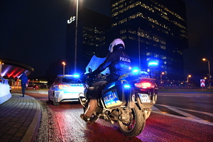 Zdjęcie kolorowe: na pierwszym planie policyjny motocykl, przed nim radiowóz, w tle budynek katowickiego spodka.
