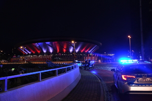Zdjęcie kolorowe: zdjęcie wykonane po zmroku, widoczne dwa policyjne radiowozy, motocykle. W tle widoczny budynek katowickiego spodka.