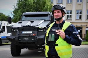 Na zdjęciu umundurowany policjant w hełmie. W tle policyjny tur.