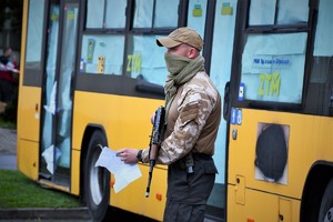 Zdjęcie. Widoczni osoba z bronią maszynową stojąca przed autobusem