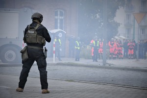 Zdjęcie. Widoczny umundurowany policjant, w tle gupa ratowników