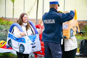 Zdjęcie. Widoczna grupa osób przebrana w kostiumy samochoidów, oraz umundurowany policjant