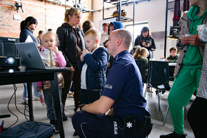 Zdjęcie. Widoczna grupa osób przy policyjnym stoisku, widoczny równiez umundurowany policjant