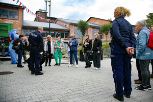 Zdjęcie. Widoczna grupa osób na placu, w tym umundurowani policjanci. Ponadto pies