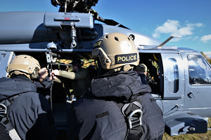 zdjęcie przedstawia policjantów zgrupowanych wokół śmigłowca, zbliżenie na kask jednego z nich.
