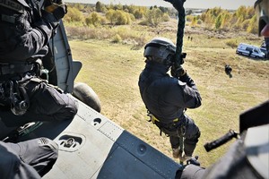 zdjęcie przedstawia policjanta desantujacego się ze śmigłowca przy użyciu liny