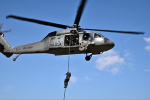 zdjęcie przedstawia policjanta desantujacego się ze śmigłowca przy użyciu liny