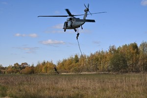 zdjęcie przedstawia policjanta desantujacego się ze śmigłowca przy użyciu liny