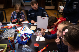 Zdjęcie.  Policjant oraz dzieci podczas tworzenia kartek świątecznych