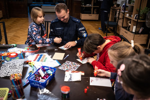 Zdjęcie.  Policjant oraz dzieci podczas tworzenia kartek świątecznych