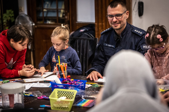 Zdjęcie.  Policjant oraz dzieci podczas tworzenia kartek świątecznych