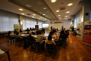Zdjęcie przedstawia grupę osób siedzących przy stołach w trakcie szkolenia w sali