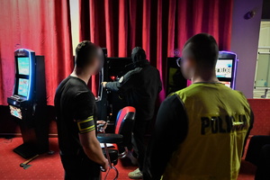 Zdjęcie przedstawia nieumundurowanych trzech policjantów wewnątrz salonu gier, którzy wykonują czynności służbowe.