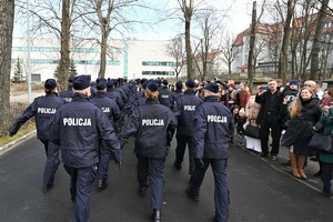 zdjęcie przedstawia przemarsz nowych policjantów w kolumnie przed swoimi rodzinami zebranymi przy drodze